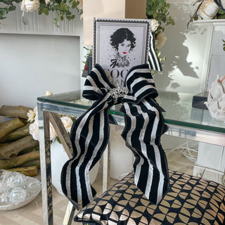 Decorative black and white striped bow on a chair with a mirror and flowers in the background
