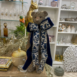 Decorative teddy bear with a large blue bow in a store setting