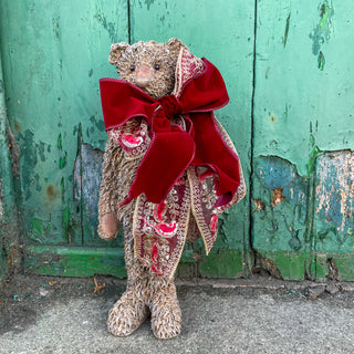 Teddy bear with a large red bow in front of a green, weathered wall