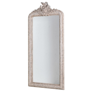 Tall French-style crest mirror in distressed antique white with ornate detailing, leaning gracefully against a wall. Available from Lily Bloom.