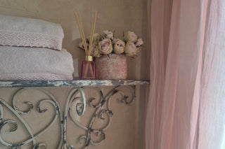Decorative elements including a vase with flowers, a towel, and a decorative metal shelf on a beige wall.