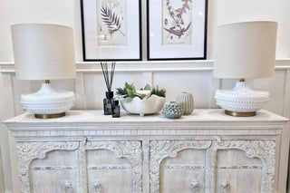 Decorative white console table with ornate carvings, two lamps, and decorative items.