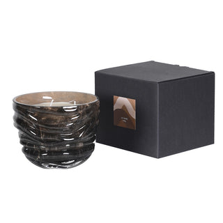 A dark brown textured glass candle with a wavy ribbed design, shown next to its black square packaging box on a white background.