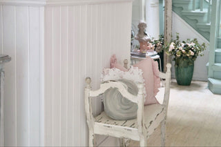Decorative interior with a white chair, framed pictures, and a vase of flowers.